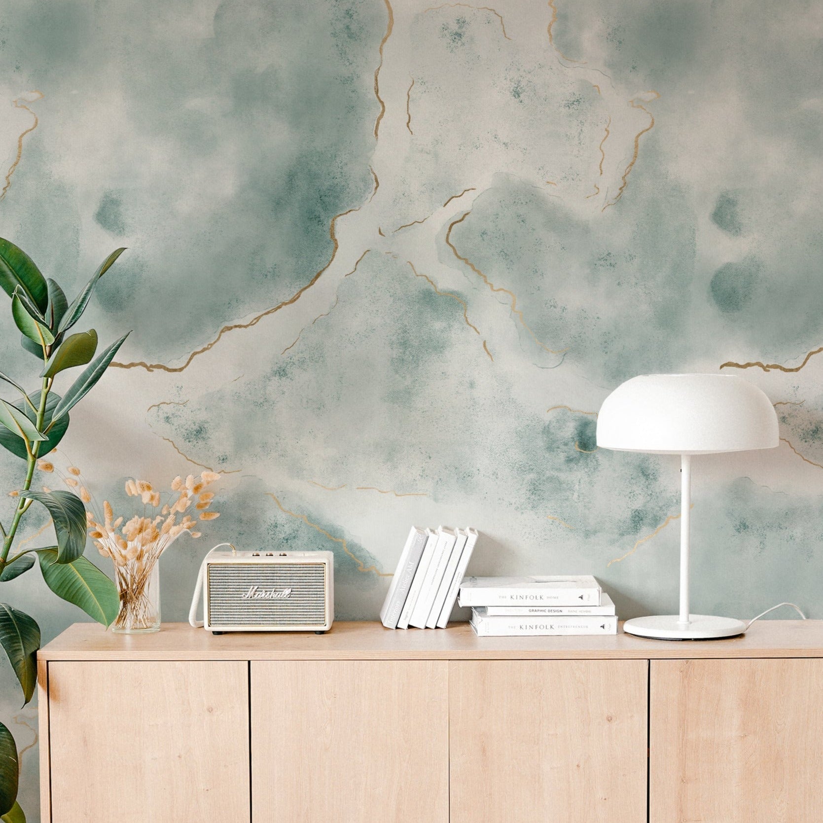 Stylish home office corner decorated with Shimmering Marble Wallpaper that exhibits a striking blue and green marble design with gold lines. The decor includes a white lamp, radio, and books on a modern wooden cabinet.