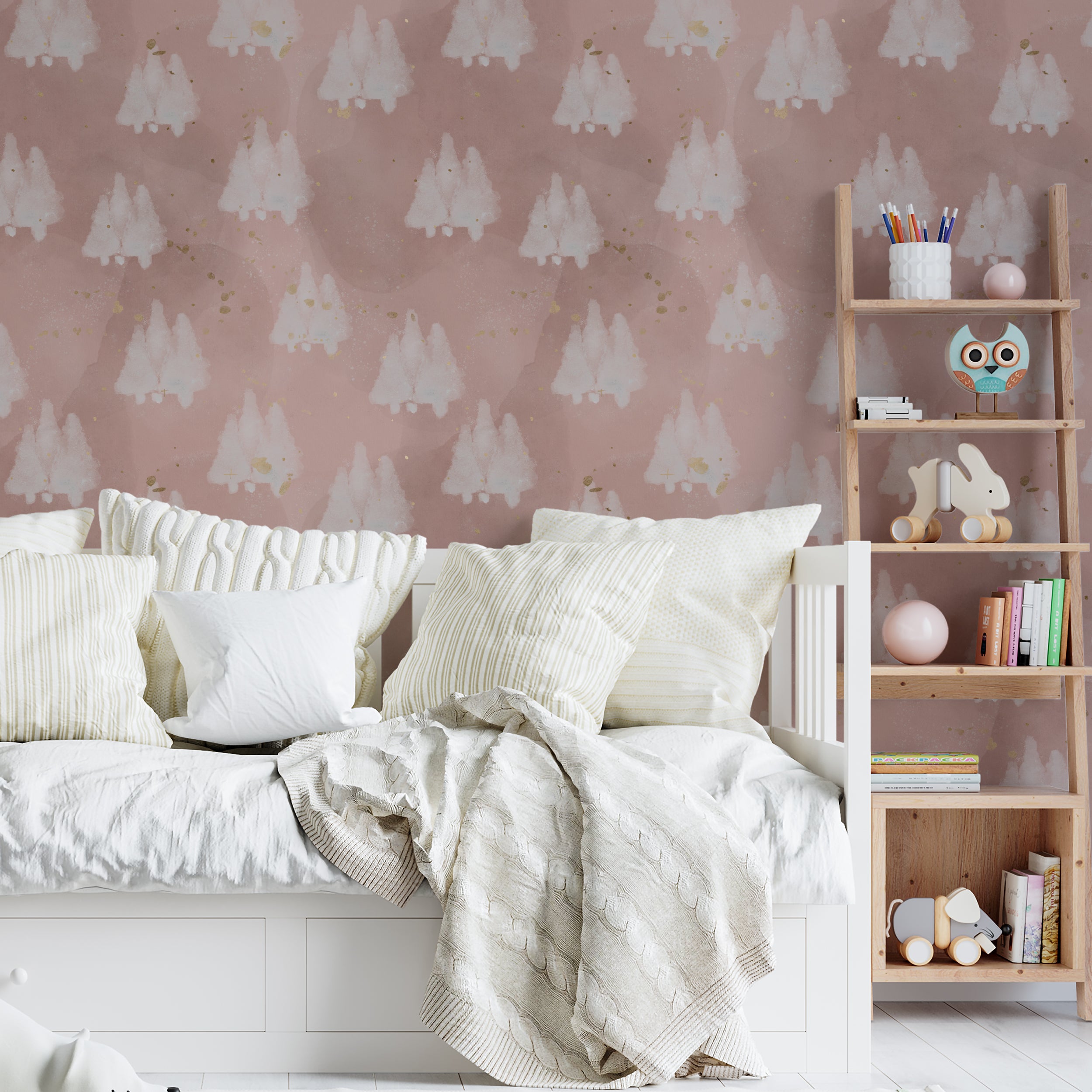 A child's bedroom displaying the Shimmer Tree Wallpaper - Pink on the walls, which portrays whimsical white trees with a snowy texture against a pastel pink backdrop, complemented by gold specks. The room is styled with cozy bedding and a playful assortment of toys and books, enhancing the room's gentle and magical atmosphere