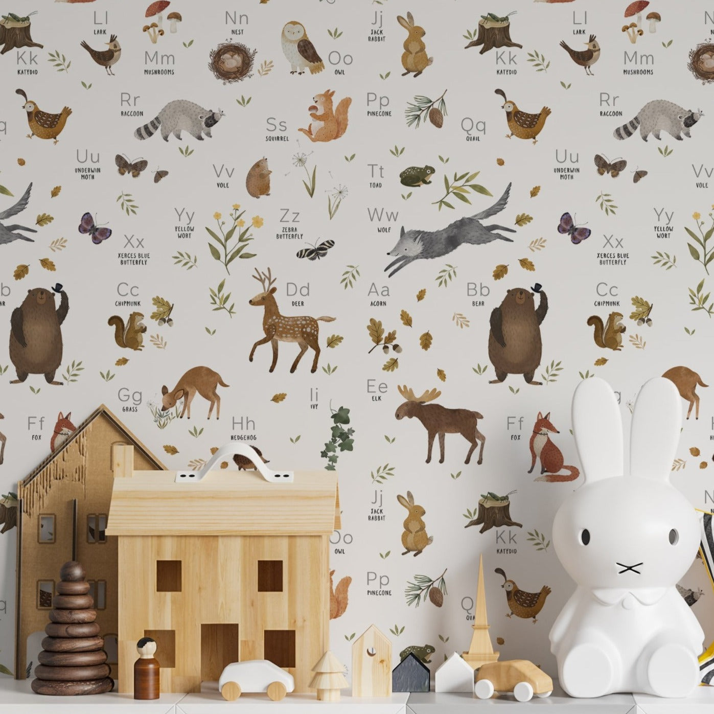 A playful children's room featuring the 'Forest Alphabet Animal Wallpaper' on the walls. The wallpaper is educational and fun, with a variety of forest animals paired with the alphabet. It forms a delightful backdrop for the white shelving unit filled with toys, creating an enchanting and stimulating environment for children.