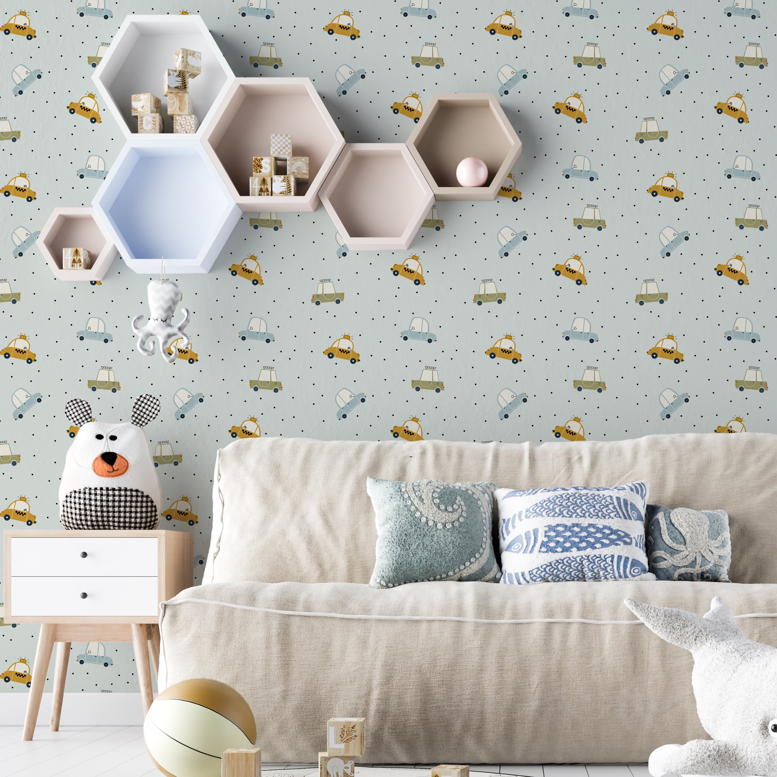 A cozy children's room setting showcasing the Cute Cars Wallpaper, with cheerful blue and yellow cars scattered across a dotted gray backdrop. The playful theme complements the room's decor, including a stuffed bear, wooden toys, and a modern, child-friendly furniture setup