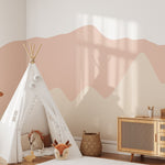 Pretty Hills Mural in a modern nursery setting with a white teepee, a plush deer toy, a wicker basket, and a wooden dresser. The mural features wavy pastel hills in calming shades of pink and beige.