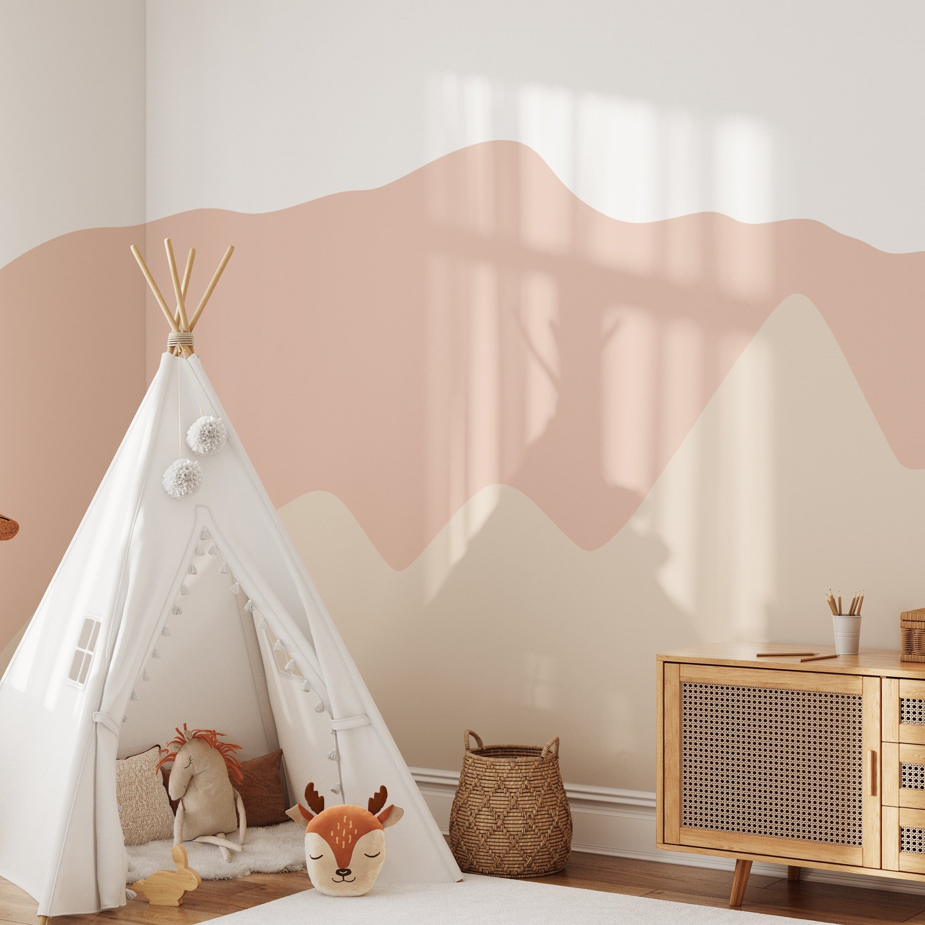 Pretty Hills Mural in a modern nursery setting with a white teepee, a plush deer toy, a wicker basket, and a wooden dresser. The mural features wavy pastel hills in calming shades of pink and beige.