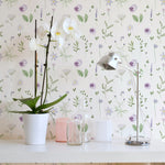 Close-up of the Wildflower Wonder Wallpaper highlighting its intricate design of purple and yellow wildflowers and green leaves. The decor includes a white orchid in a pot and a sleek metallic desk lamp on a white desk