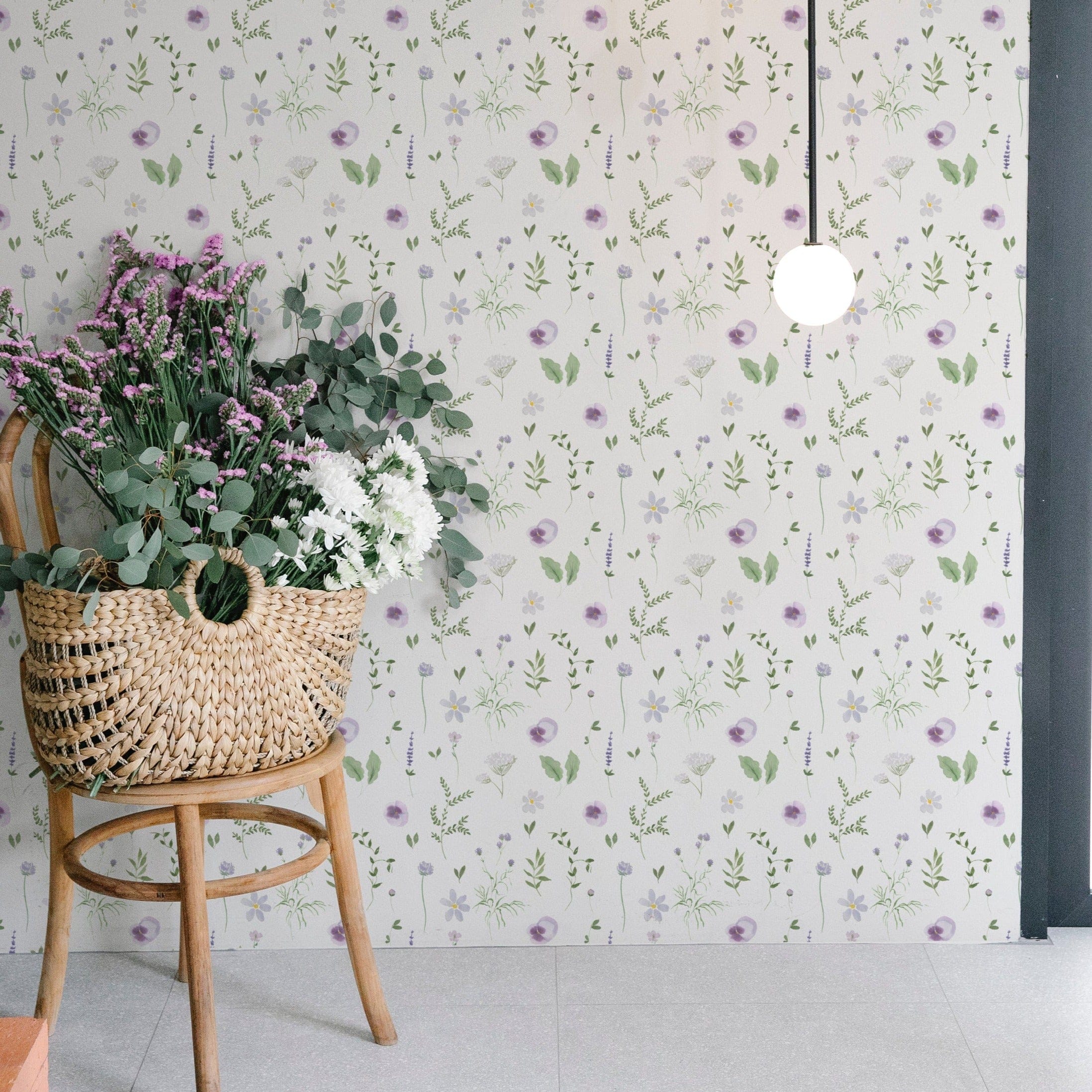 A corner of a room with the Wildflower Wonder Wallpaper, displaying its beautiful pattern of purple and yellow wildflowers. The decor features a woven basket filled with flowers and a hanging light