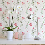 Close-up of the Spring Serenity Wallpaper showcasing its pattern of pink flowers and green leaves, enhancing the room's decor with a white orchid in a pot and a sleek metallic desk lamp