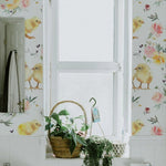 A bathroom decorated with 'Spring Animal Watercolour Wallpaper' showcasing cheerful yellow chicks and floral designs, complementing a white interior with natural greenery.