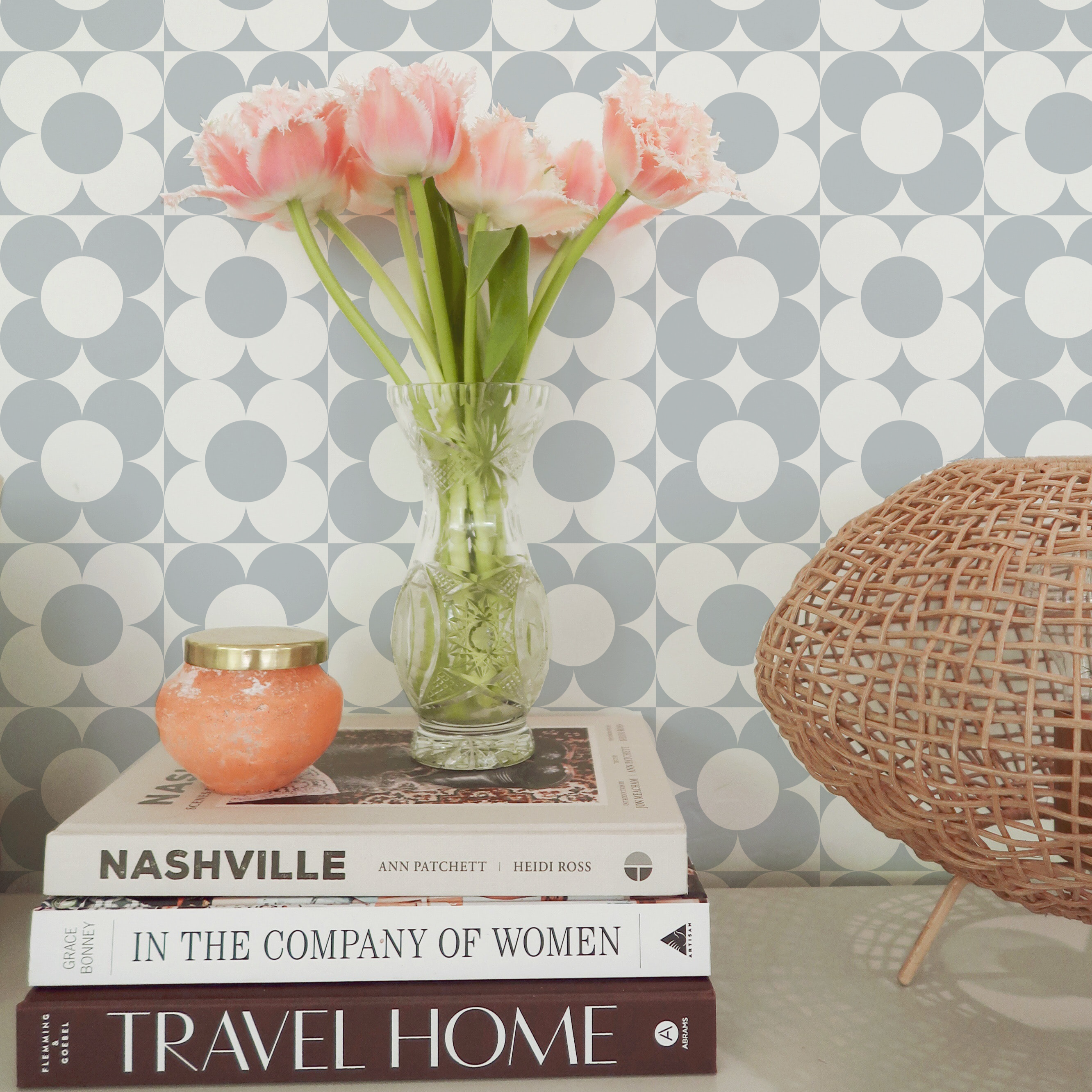 Elegant home decor setup with Vintage Groovy Wallpaper - Pale Blue as a backdrop, featuring a vase of fresh pink tulips, a rattan chair, and a stack of books, creating a chic and inviting atmosphere.