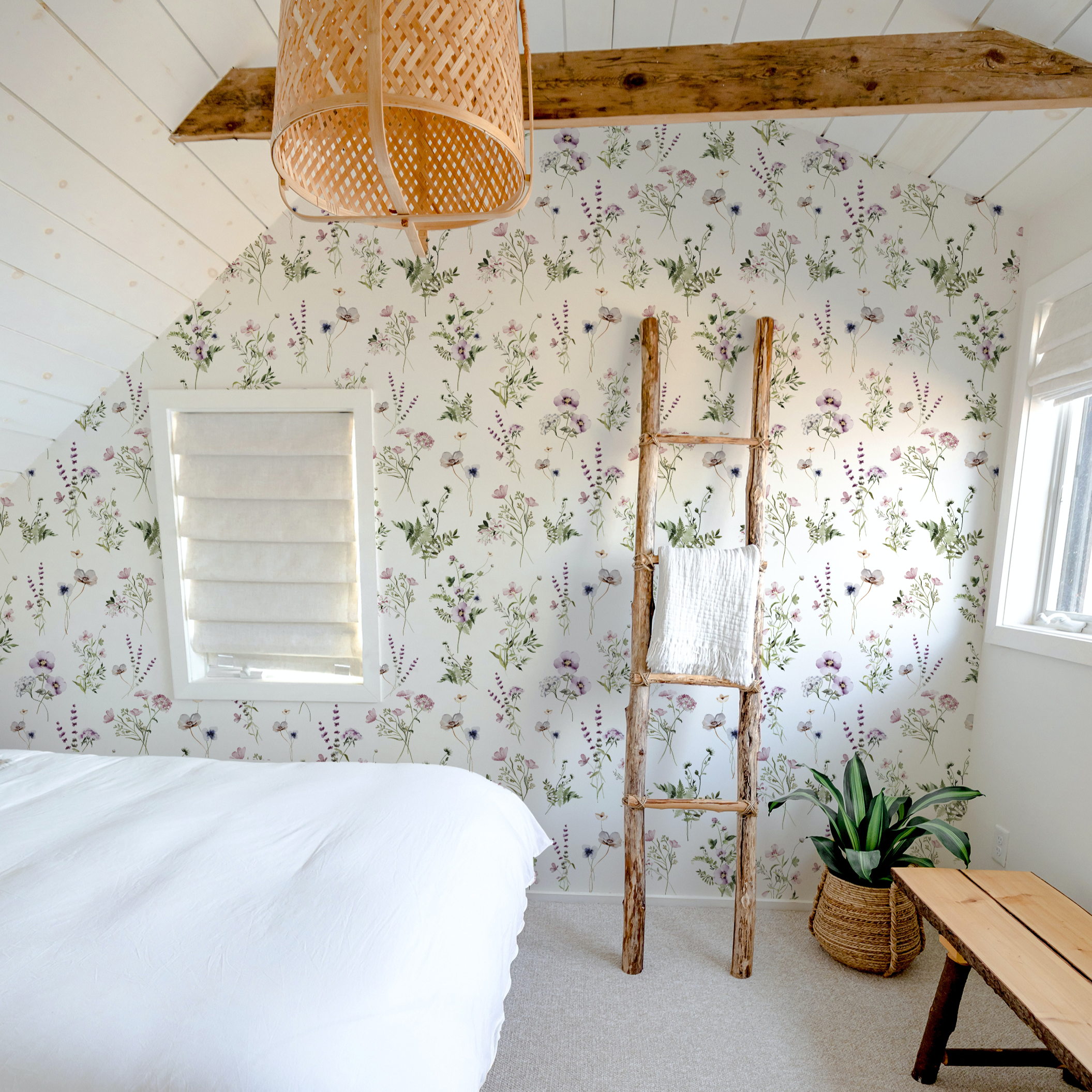 The 'Midsummer Watercolour Bouquet Wallpaper - Raspberry' enhances the bright and airy ambiance of a bedroom, complemented by natural elements like a rustic ladder and woven light fixture, creating a charming and restful space.