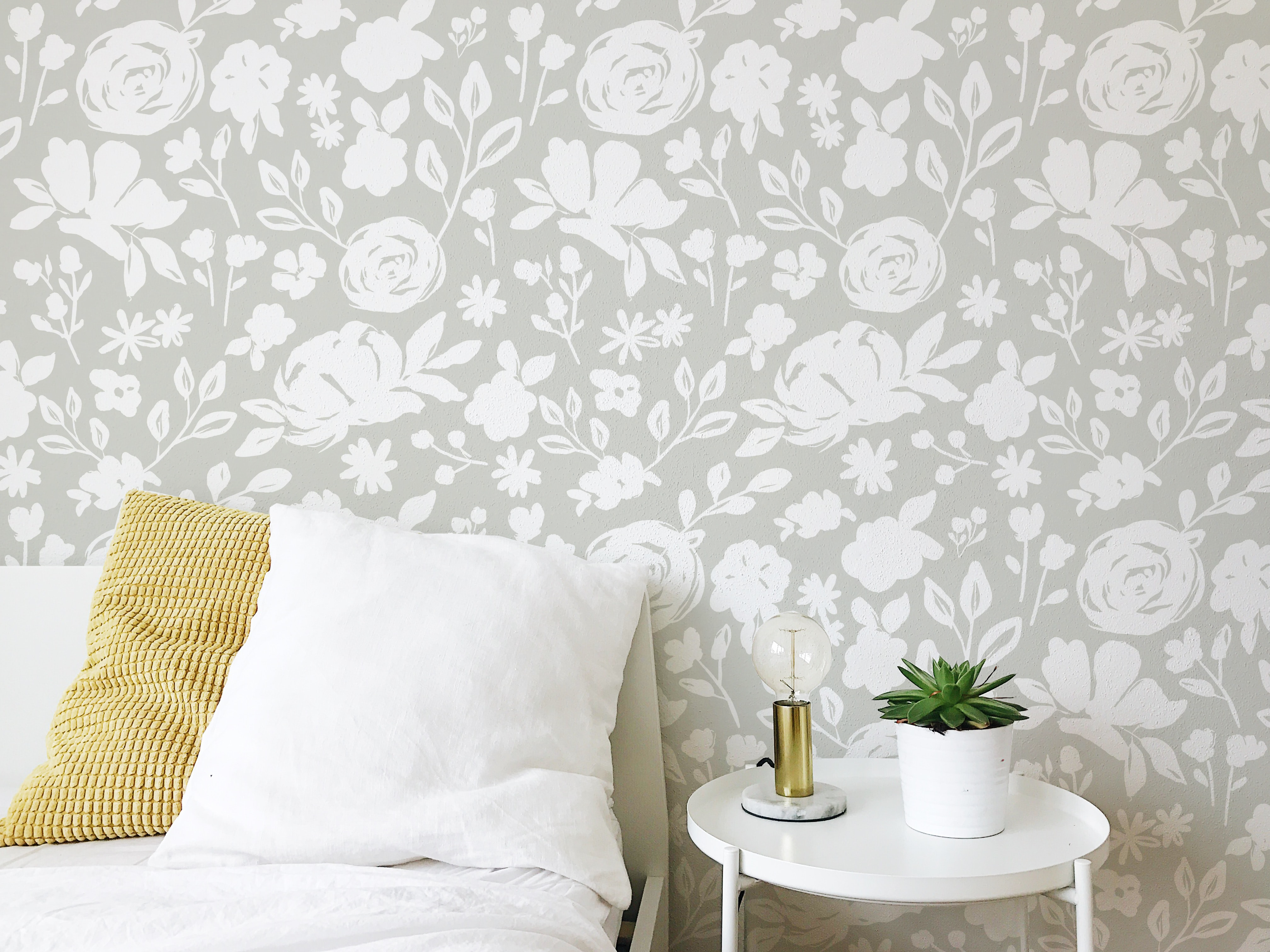 Part of a cozy bedroom with a corner displaying 'Silhouette Floral Wallpaper - Silk Green', which features elegant white floral silhouettes on a soft green background, providing a fresh and serene ambiance