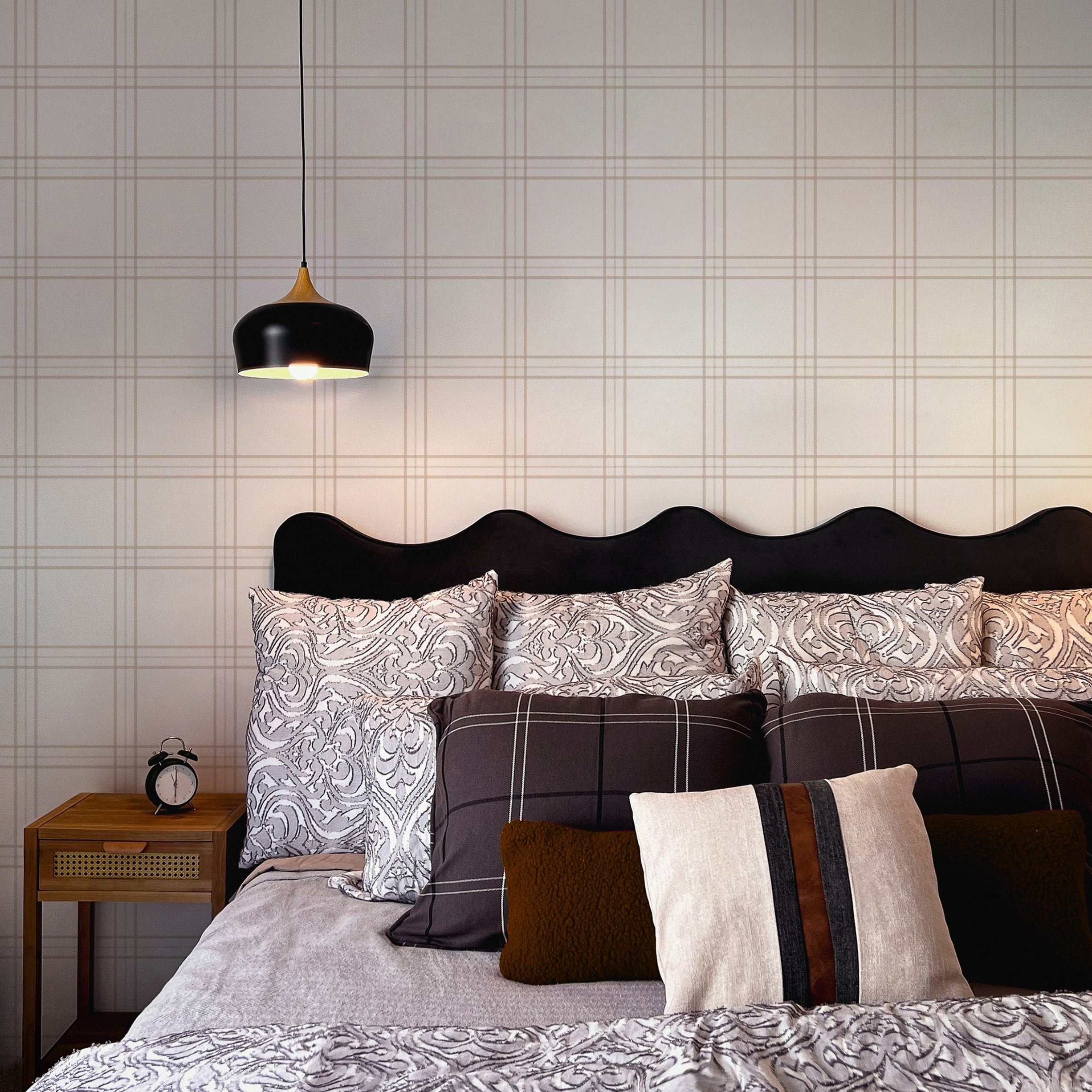 An elegant bedroom interior where the Traditional Tartan Plaid Wallpaper adds a subtle yet impactful backdrop to the stylish monochrome bedding and dark, curvaceous headboard, harmoniously paired with a modern black pendant light and wooden nightstand.