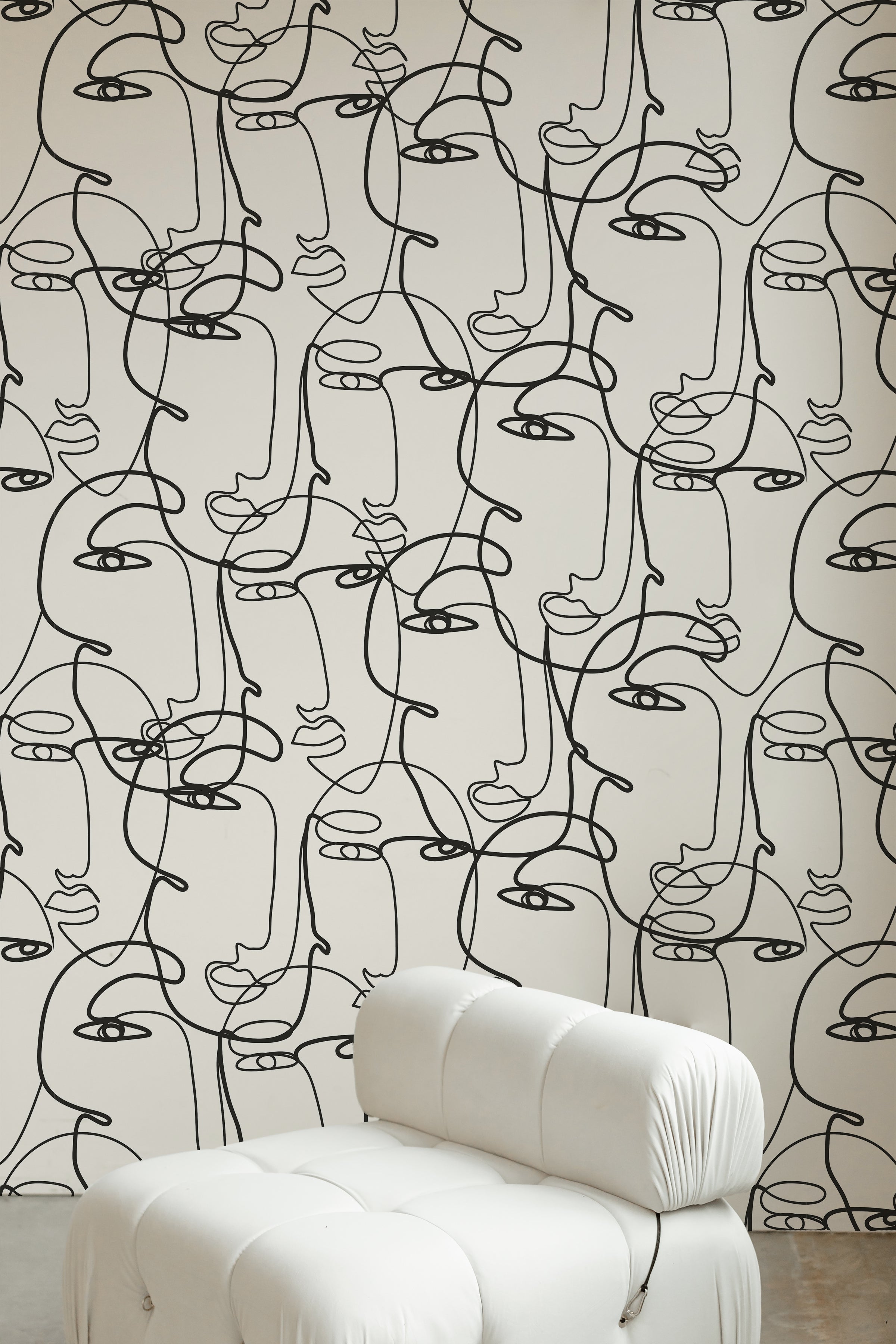 A stylish living area with Minimalist Faces Wallpaper featuring a black line art pattern of abstract faces on a white background. The decor includes a white, tufted chair, adding a touch of elegance to the space.