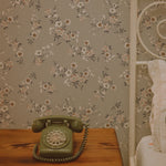 A vintage bedroom corner with the Classic Floral Wallpaper providing a nostalgic backdrop. The wallpaper’s floral pattern exudes a timeless grace, paired with a retro green telephone on a wooden nightstand. The soft hues and floral design enhance the room's romantic and historical ambience.