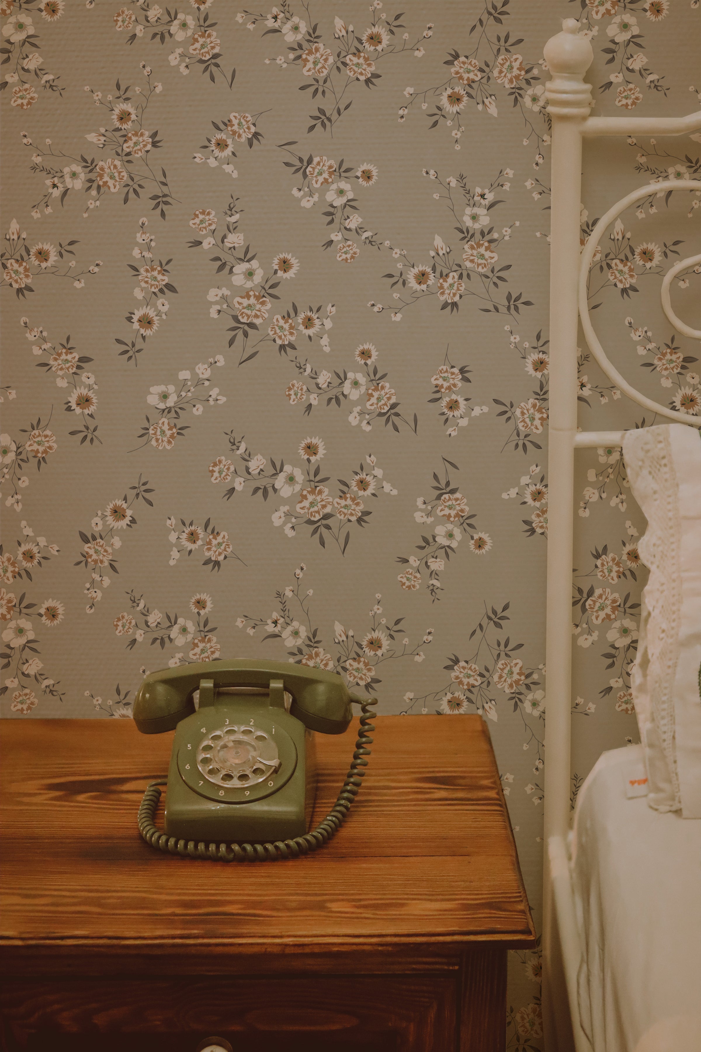 A vintage bedroom corner with the Classic Floral Wallpaper providing a nostalgic backdrop. The wallpaper’s floral pattern exudes a timeless grace, paired with a retro green telephone on a wooden nightstand. The soft hues and floral design enhance the room's romantic and historical ambience.