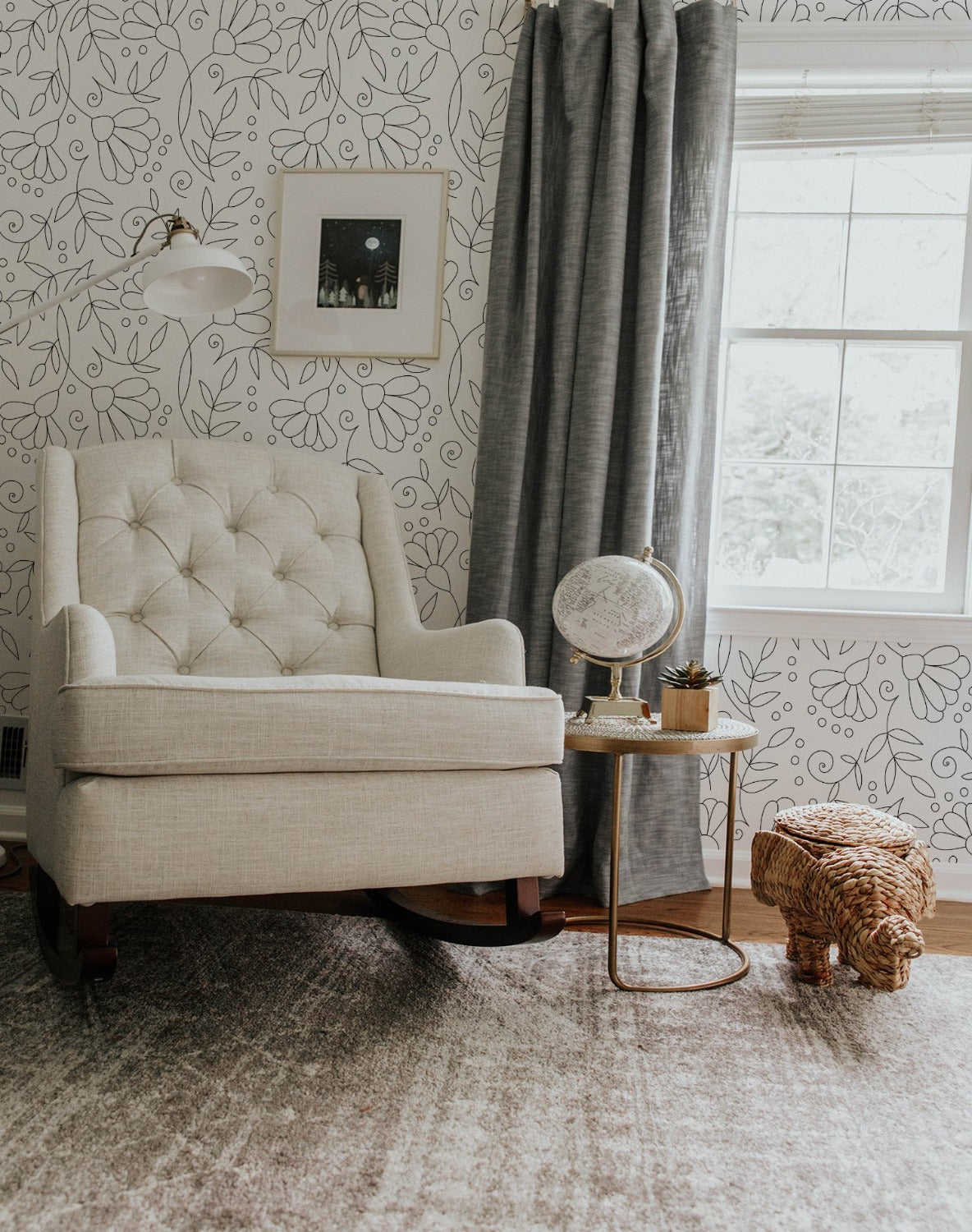 A cozy reading corner with the Simple Black Floral Wallpaper accentuating the wall behind a tufted beige armchair, a rustic globe table lamp, and wicker animal-shaped basket, creating a charming and inviting space