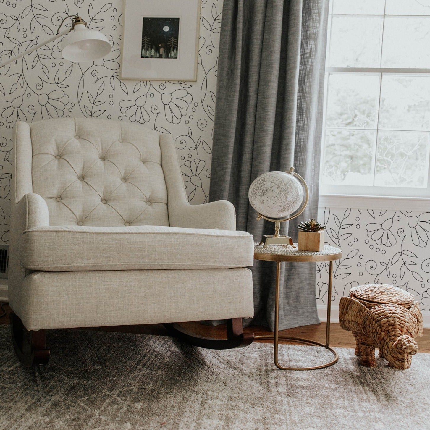 A cozy reading corner with the Simple Black Floral Wallpaper accentuating the wall behind a tufted beige armchair, a rustic globe table lamp, and wicker animal-shaped basket, creating a charming and inviting space