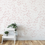 A room corner with Pink Floral Wallpaper as a backdrop. The wallpaper features a soft pink leafy pattern on a white background. The decor includes white shelves with potted plants, enhancing the delicate and natural ambiance.