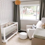 A well-lit, tranquil nursery room featuring 'Minimal Line Wallpaper' on one wall, complemented by a white crib, gray curtains, and a comfortable armchair, creating a soothing and chic environment.