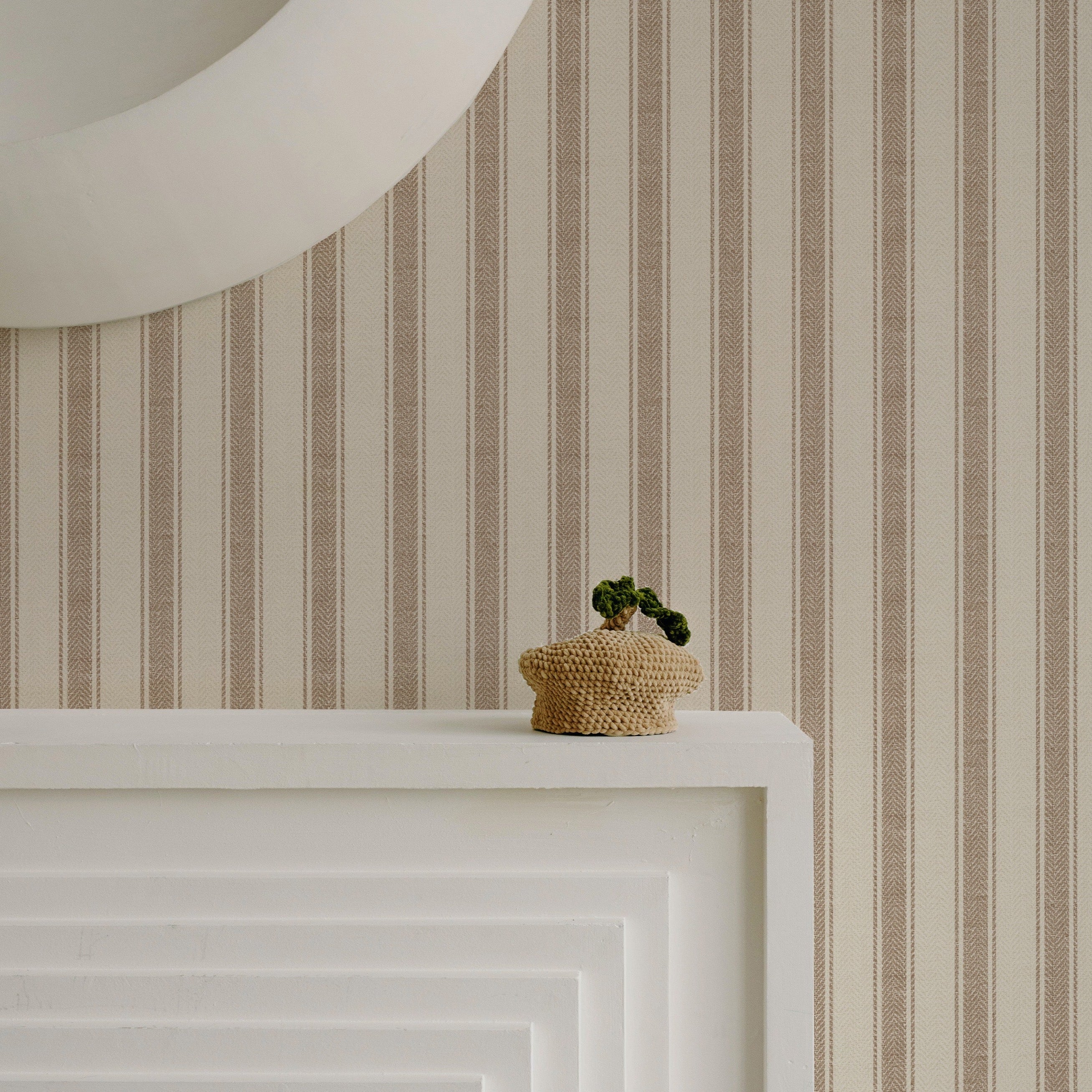 A minimalist detail shot showing the Striped Fabric Wallpaper above a white mantelpiece, where a small woven basket with a houseplant sits, highlighting the wallpaper's subtle texture and elegant stripe pattern.