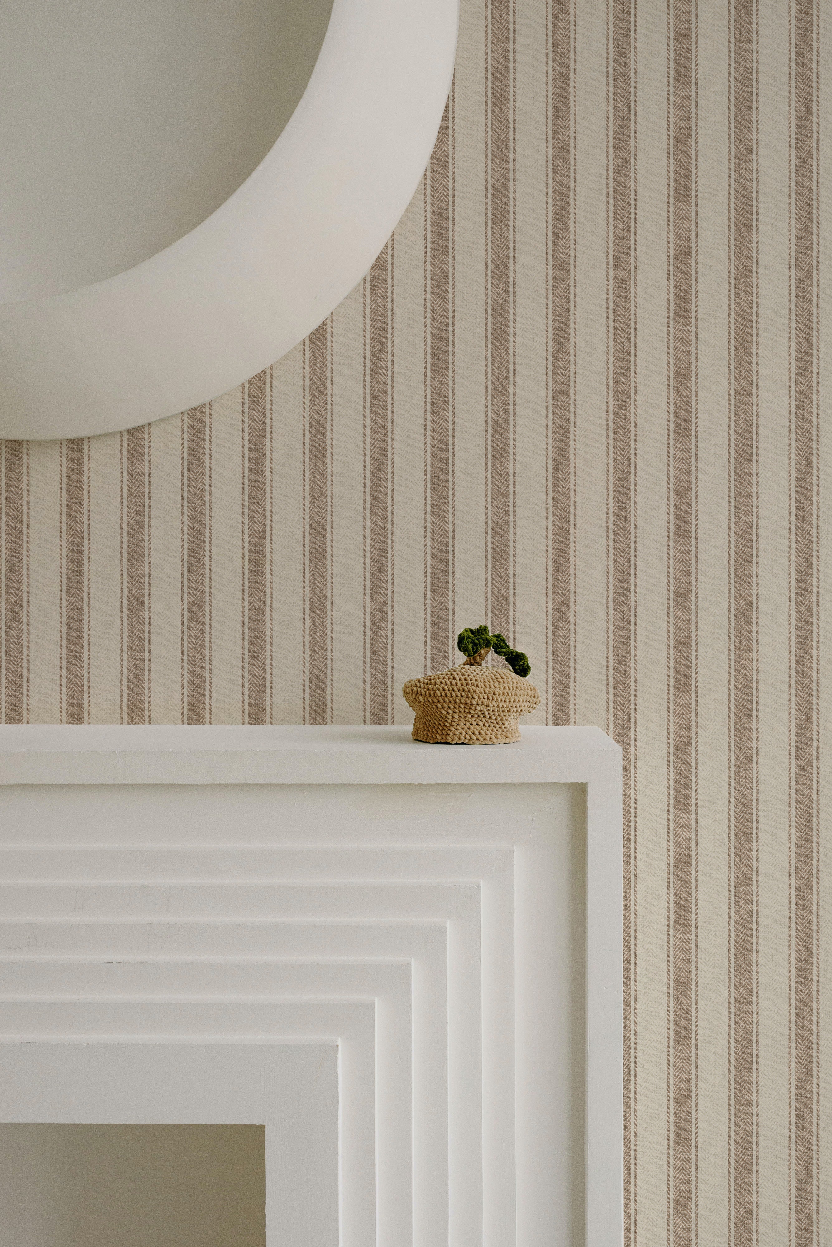 A minimalist detail shot showing the Striped Fabric Wallpaper above a white mantelpiece, where a small woven basket with a houseplant sits, highlighting the wallpaper's subtle texture and elegant stripe pattern.