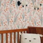 The wallpaper with a whimsical flower pattern is applied in a nursery room, adorning the wall behind a wooden crib. A plush sheep toy peeks out from the crib, complementing the gentle and nurturing ambiance of the room.