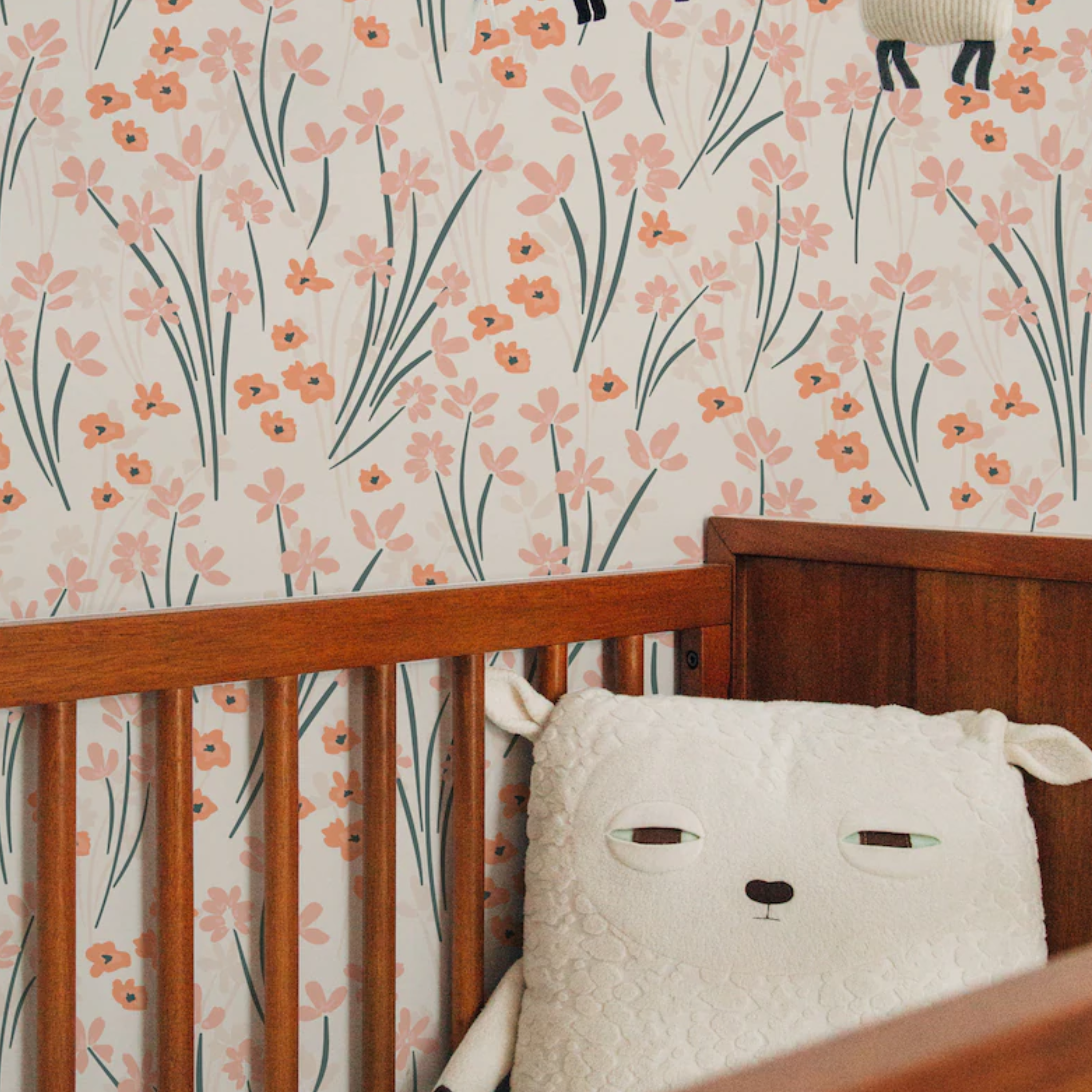 The wallpaper with a whimsical flower pattern is applied in a nursery room, adorning the wall behind a wooden crib. A plush sheep toy peeks out from the crib, complementing the gentle and nurturing ambiance of the room.