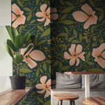 A chic dining area with 'Floral Love Watercolour Wallpaper' providing a captivating dark backdrop adorned with large watercolor pink blossoms and leaves, complemented by natural wood furniture and lush green plants