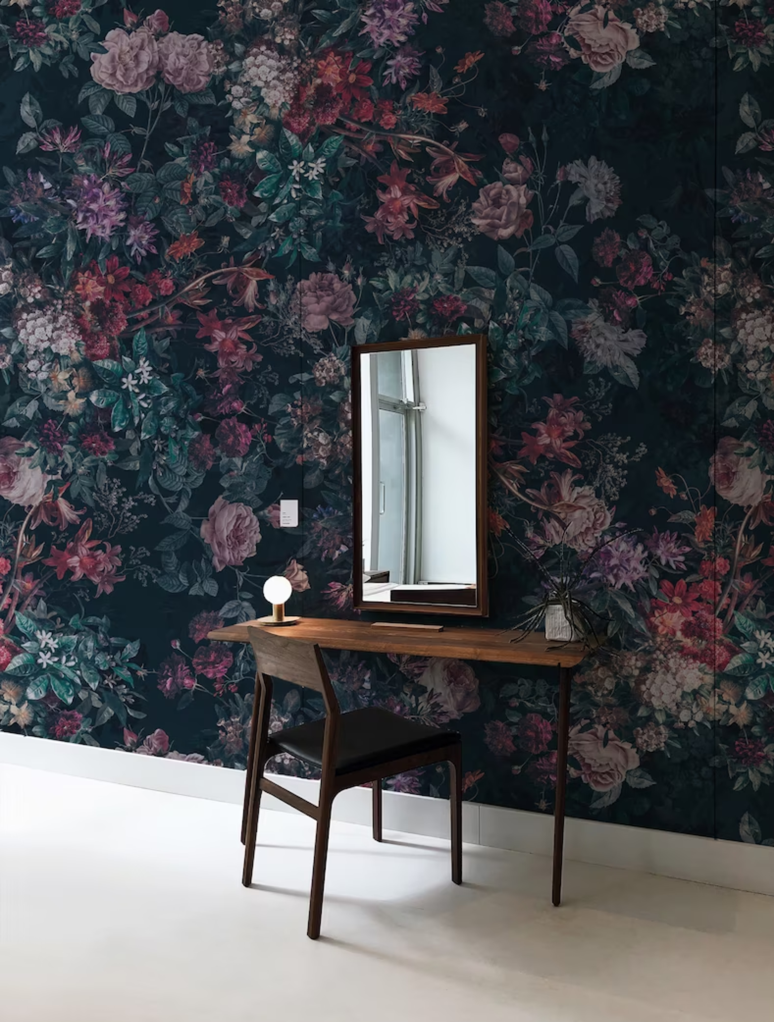 A stylish entryway is enhanced by the Dark Luxury Floral Wallpaper - Large, featuring bold floral patterns in rich hues on a dark backdrop, complemented by a sleek wooden console table, a classic mirror, and minimalistic decor, creating an ambiance of sophisticated allure.