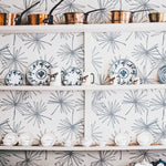 A kitchen scene featuring Line Minimal Floral Leaf wallpaper, with a sketched design of thin-lined floral leaves in blue on a white background. Above a white shelf holding decorative plates and mugs, copper pots and pans hang, adding a rustic charm against the contemporary floral backdrop.