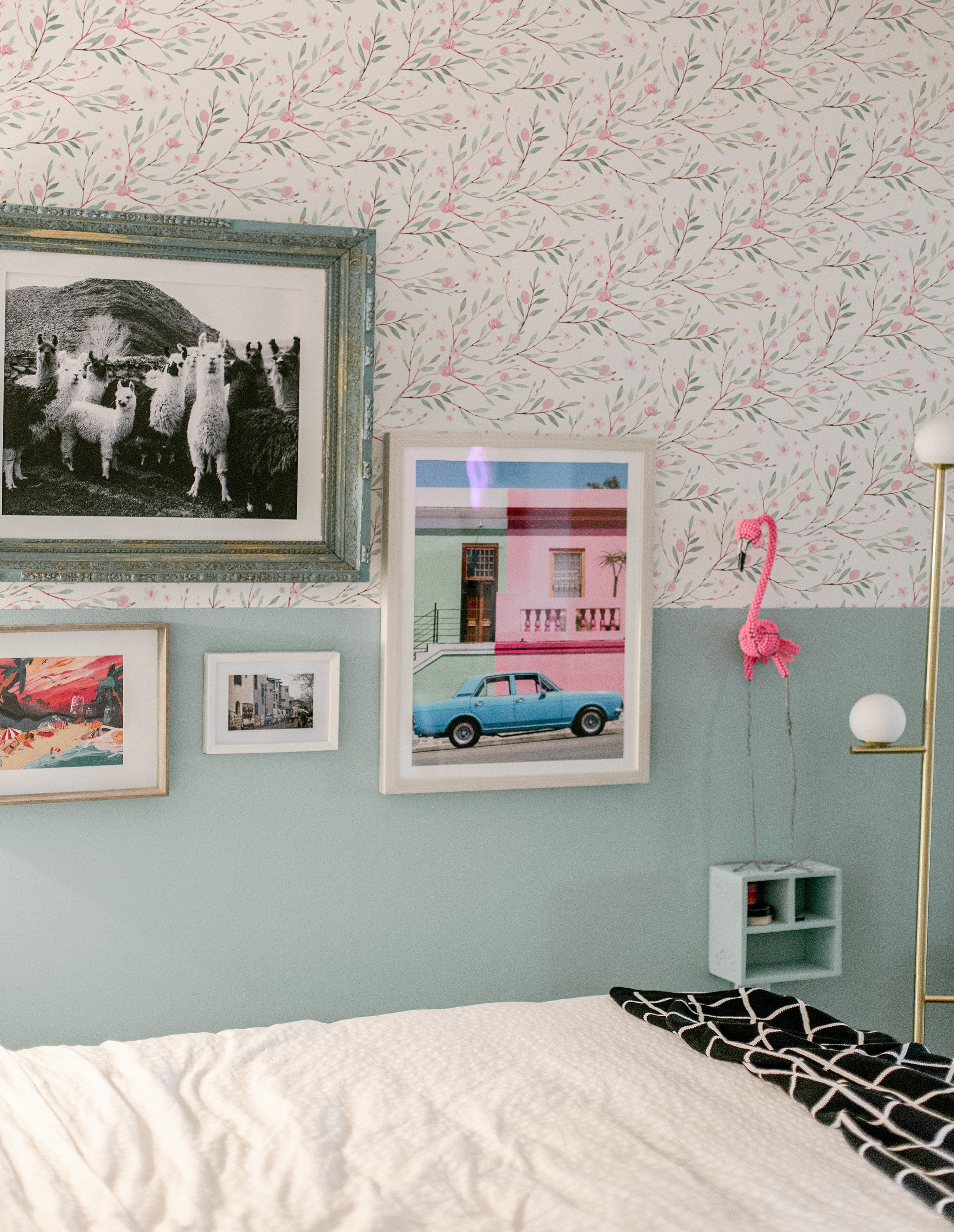 A stylish bedroom decorated with Watercolour Spring Bird Wallpaper - Multi, enhancing the room's charm with its soft floral pattern amid eclectic framed pictures, creating a cozy and inviting atmosphere.