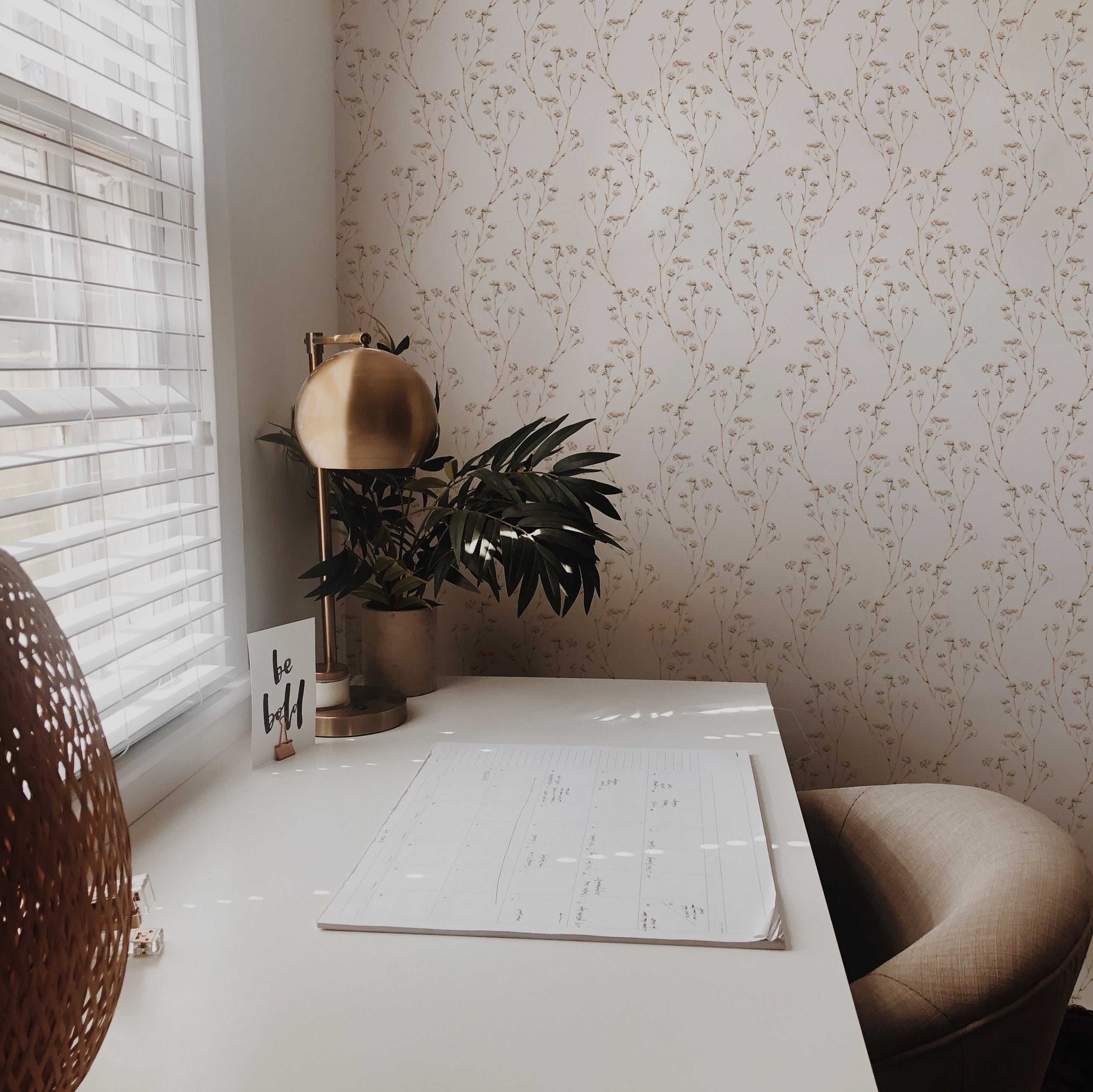 A well-lit office corner with 'Boho Branches Wallpaper' featuring a delicate, neutral-toned branch pattern, complementing the modern desk and brass desk lamp, creating a calm and inviting workspace