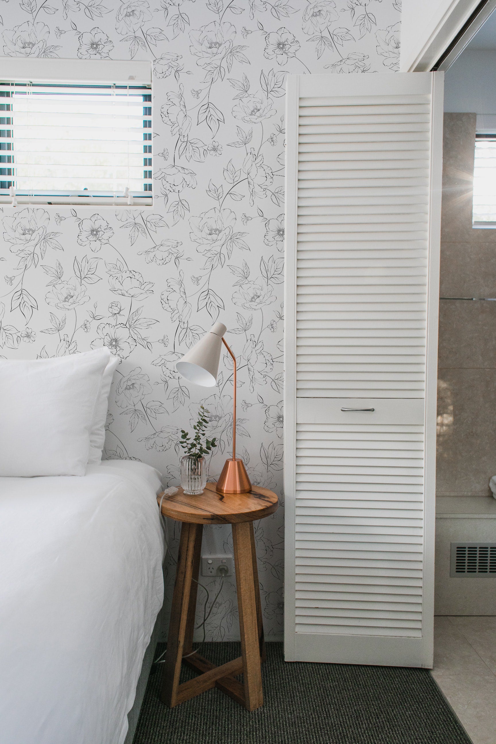 Cozy bedroom corner with Dainty Floral Line Wallpaper, showcasing a laptop on a bed with white linens and fresh flowers