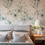 A stylish bedroom featuring the Green Leaves and Branches Wallpaper - Large, with an elegant botanical design of green leaves and branches that brings a sense of nature's serenity to the room, complemented by textured gray bedding and a chic bedside table with a vase and lamp.