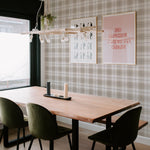 A contemporary dining area accented with Winter Plaid Wallpaper, featuring a solid wood table with velvety green chairs. The wallpaper's plaid pattern provides a timeless backdrop, harmoniously blending with the modern furnishings and light-hearted wall art.