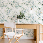 A bright and airy workspace with Green Leaves and Branches Wallpaper, wooden desk, and director's chair creating a refreshing indoor atmosphere.