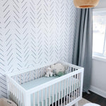 A well-lit, tranquil nursery room featuring 'Minimal Line Wallpaper' on one wall, complemented by a white crib, gray curtains, and a comfortable armchair, creating a soothing and chic environment.
