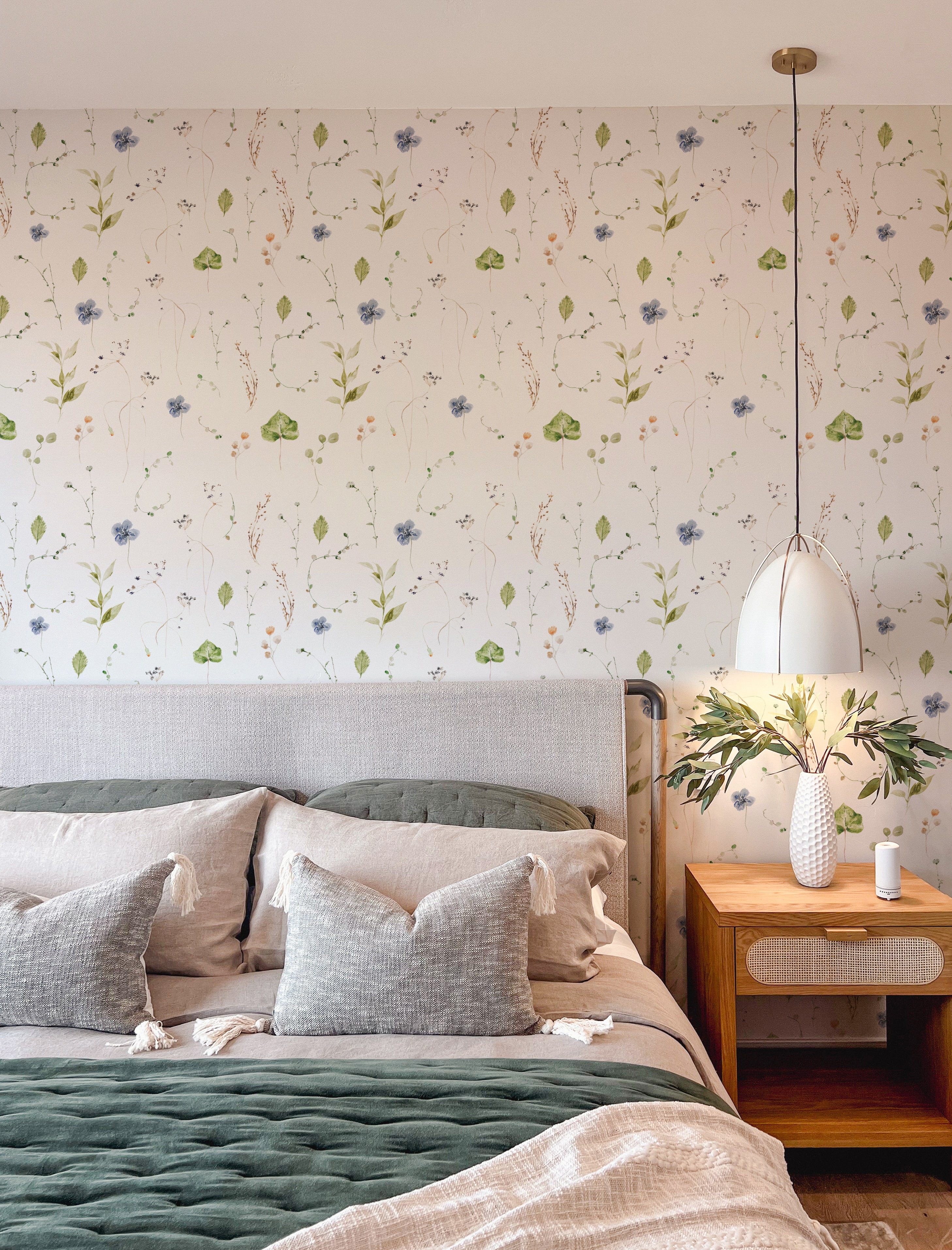 A cozy bedroom with 'Ikebana Floral Wallpaper' enhancing the wall behind a bed with plush green and gray pillows, with the natural floral pattern contributing to a restful ambiance.