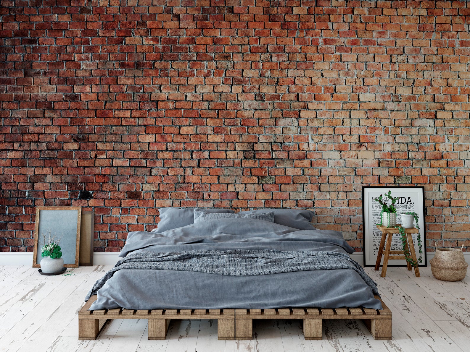 A stylish bedroom setting with Realistic Red Brick Wallpaper as a statement wall behind a bed with grey linen and a wooden pallet base. The brick wall adds a cozy and industrial charm to the room.