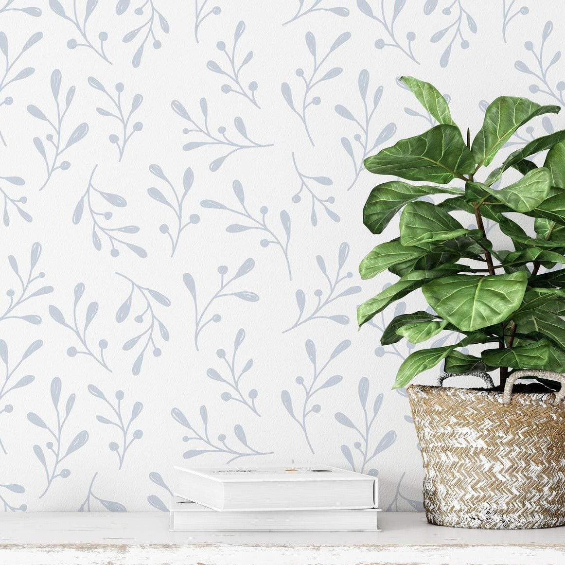 A lifestyle scene with the Natural Wallpaper II adorning a wall behind a lush green potted plant sitting atop a white book on a wooden floor. The botanical grey sprigs on the wallpaper bring a naturalistic and tranquil vibe to the space.