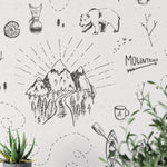 A whimsically designed bedroom with the Big Adventure Kids Wallpaper depicting a black and white illustrated scene of outdoor activities and wildlife, including bears, tents, mountains, and trees, which creates a playful and adventurous vibe.