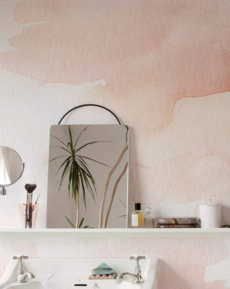 A closer view of the abstract Hand Painted Mural Wallpaper in a bathroom setup, exhibiting a blush watercolor effect, providing a subtle yet artistic backdrop to the modern white sink and sleek bathroom accessories.