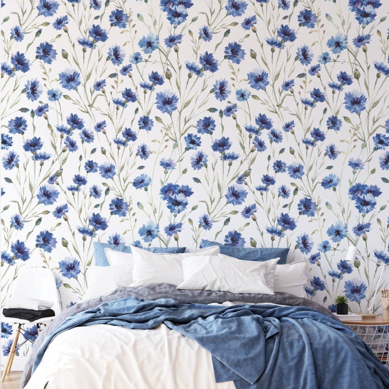 A bedroom with the 'Hand Painted Blue Floral Wallpaper' providing a striking statement behind a simple bed dressed in white and blue linens, blending artistic flair with a calming sleeping environment