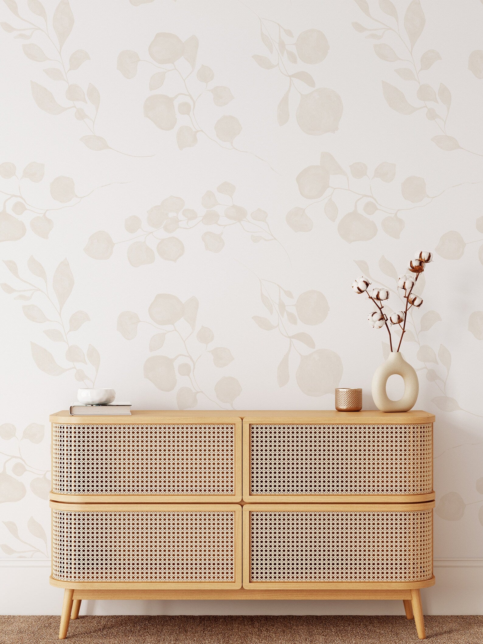 A minimalist modern room showcasing the 'Subtle Botanique Wallpaper', with soft beige botanical silhouettes complementing the clean lines of a rattan-fronted sideboard, adorned with a simple vase and books, enhancing the room's serene and chic vibe