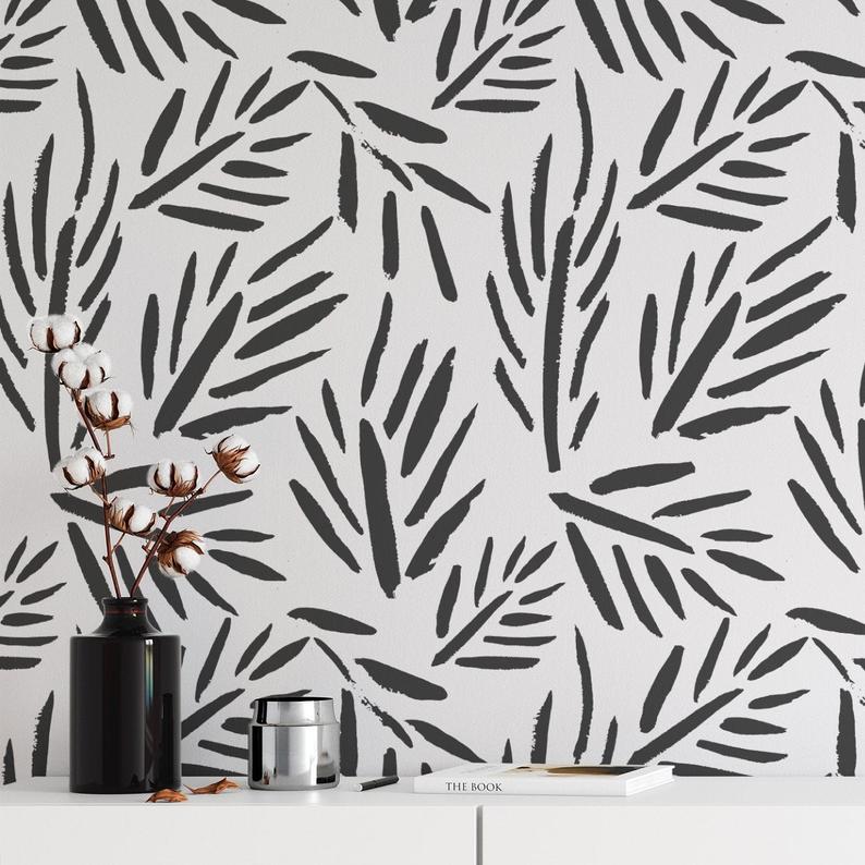A stylish interior featuring a wall adorned with 'Black Floral Wallpaper - Modern Abstract', showcasing a bold black and white pattern of abstract foliage. A vase with cotton stems, a metallic silver container, and a book titled 'THE BOOK' sit on a sleek white sideboard against the wallpaper, presenting a chic and contemporary look.