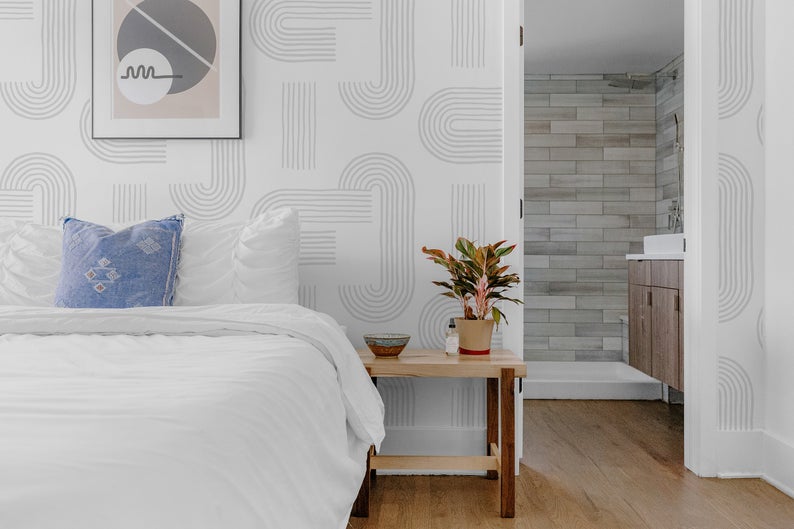 A modern minimalist bedroom featuring the 'Zen Abstract Wallpaper II', with a sophisticated grey and white abstract design on the wall, complemented by simple bedding, a blue decorative pillow, and contemporary framed artwork.
