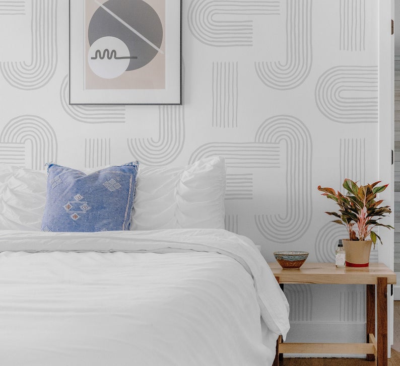 A modern minimalist bedroom featuring the 'Zen Abstract Wallpaper II', with a sophisticated grey and white abstract design on the wall, complemented by simple bedding, a blue decorative pillow, and contemporary framed artwork.