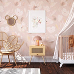 A charming nursery featuring the Prettiest in Pink Floral Wallpaper, with soft pink blooms and delicate foliage on a light background, complemented by a whimsical rattan peacock chair, a delicate white canopy over a crib, and playful children's decor, creating a serene and enchanting space for a little one.