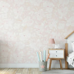 Child's bedroom with a wall adorned in Soft Pastel Pink Floral Wallpaper featuring subtle pink watercolor flowers, complemented by wooden furniture and a star-themed bedspread.