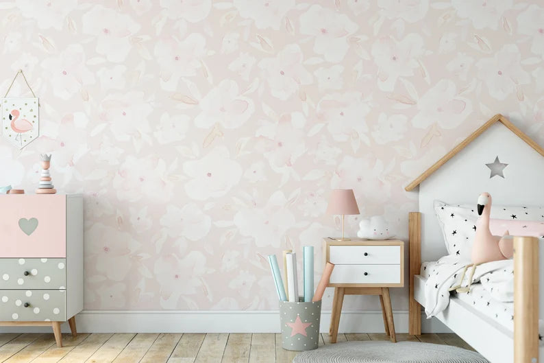 Child's bedroom with a wall adorned in Soft Pastel Pink Floral Wallpaper featuring subtle pink watercolor flowers, complemented by wooden furniture and a star-themed bedspread.