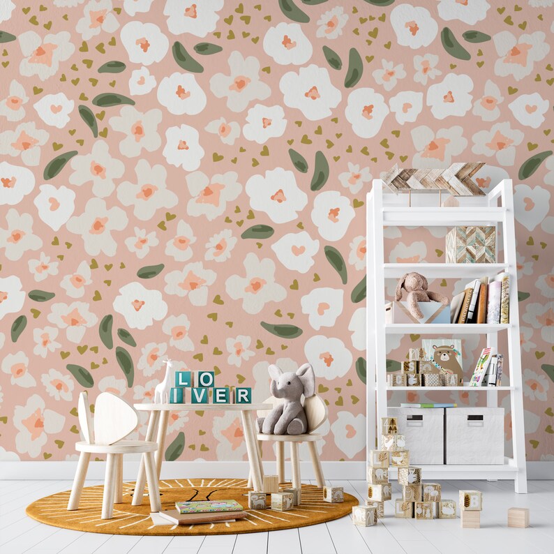 A children's play area adorned with the Beautiful Pink Abstract Floral Wallpaper that features a whimsical pattern of soft pink flowers and green foliage on a gentle pink backdrop, complementing the white furniture and playful decor
