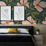 A contemporary bedroom with 'Floral Love Watercolour Wallpaper' in vibrant hues, showcasing oversized pink flowers and lush greenery on a dark background, accented by modern line art portraits above a plush bed with a bold yellow pillow.